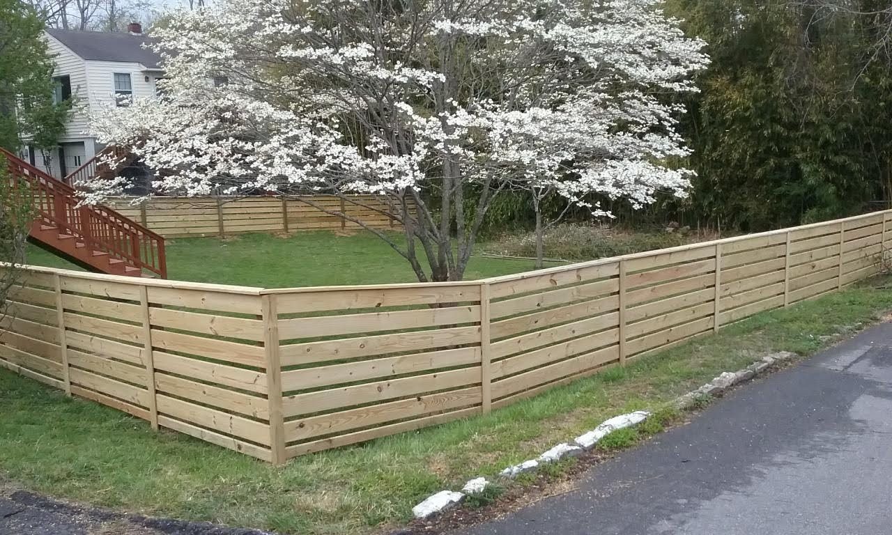 Horizontal board wood fence corner under a flowering dogwood, built by Big Boy Fencing