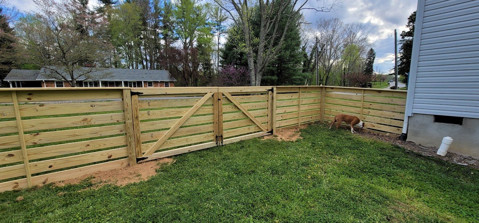 Horizontal board wood fence with a double gate beside a house